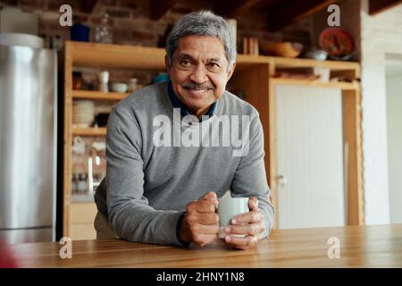 Portrait d'un homme âgé biracial à la retraite, penché sur le comptoir de cuisine, souriant à l'appareil photo. Banque D'Images