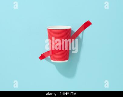 gobelet en carton rouge collé avec du ruban adhésif rouge sur le fond bleu Banque D'Images