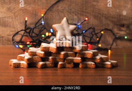 Des étoiles de cannelle empilées sur une table en bois avec des lumières de Noël colorées Banque D'Images