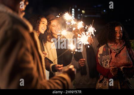 Groupe multiculturel d'amis riant tout en éclairant des amateurs lors d'une soirée sur le toit à la mode Banque D'Images