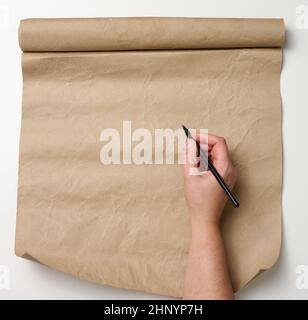 la main femelle tient un crayon de bois sur un rouleau de papier brun sur une table blanche.Place pour écrire du texte, liste Banque D'Images