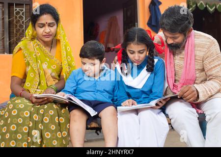 Parents indiens traditionnels aidant leurs jeunes enfants dans les études, garçon et fille dans l'uniforme scolaire étudiant à la maison. Mère portant sari et le père dedans Banque D'Images