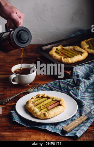 Mini-galette rhubarbe sur plaque blanche. À la main, avec une cafetière à piston Banque D'Images