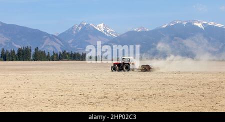 Le tracteur tirant plus de rouleaux de printemps sec dans les champs, les montagnes avec peu de neige en arrière-plan. Banque D'Images