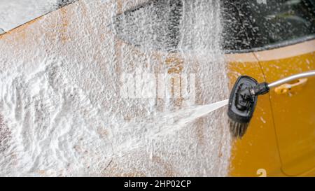 Voiture jaune lavé au carwash - shampooing mousse épaisse et blanche sur le côté arrière splutter. L'espace pour le texte sur la gauche. Banque D'Images