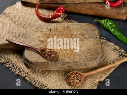 cuisine vide, planche à découper en bois brun sur table noire, à côté de cuillères aux épices et au piment frais, fond noir Banque D'Images