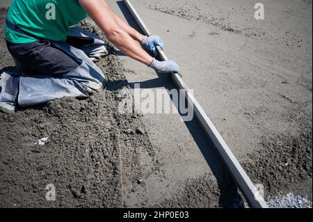 Gros plan du carrossier plaçant le rail de table sur le plancher recouvert de mélange sable-ciment sur le chantier de construction sur le toit. Surface de nivellement pour homme avec bord droit lors du crier le sol. Banque D'Images