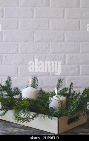 Composition floristique de Noël simple avec des bougies et des branches de sapin sur un fond de mur de brique blanche. Copier l'espace Banque D'Images