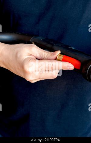 Gros plan de l'homme chargeant une carapace de fusil de chasse rouge dans le magazine de son arme. Charger une arme Smoothbore à pompe Banque D'Images