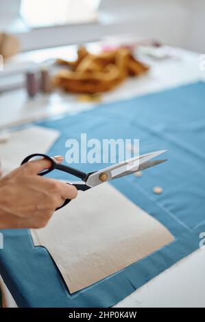 Une couturière avec ciseaux coupe un motif en tissu sur son lieu de travail en atelier. Couture professionnelle et couture professionnelle, confection artisanale, Banque D'Images