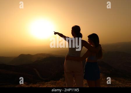 Silhouette rétro-lumineuse de deux femmes montrant le soleil au coucher du soleil Banque D'Images