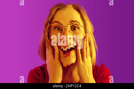 Génial. Belle surprise excitée fille isolée sur néon violet studio backgroud. Jeune femme debout avec la bouche ouverte. Effet destructeur Banque D'Images