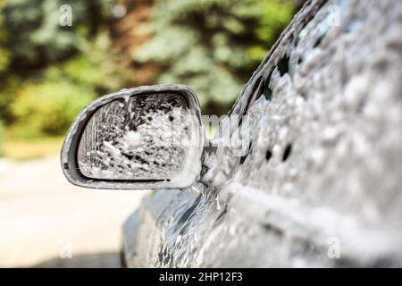 Le rétroviseur de voiture d'argent, couvertes de mousse et de shampooing, au lavage en lave-auto sur une journée ensoleillée. Banque D'Images