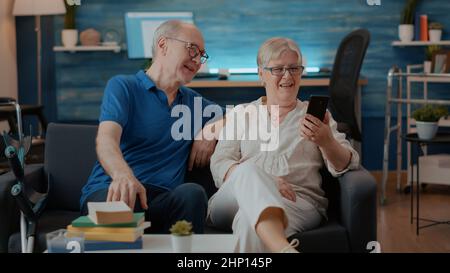 Un couple retraité parle à sa famille lors d'un appel vidéo à distance, en utilisant un smartphone pour les télécommunications. Homme et femme âgés qui discutent par téléconférence en ligne. Discussion sur Internet Banque D'Images