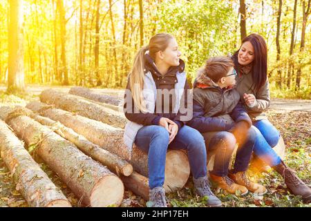 La famille avec mère et deux enfants est assise dans la forêt sur des bûches décortiquées en été Banque D'Images