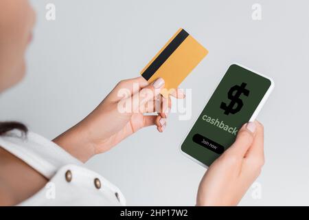 vue partielle d'une femme utilisant un téléphone portable avec cashback à l'écran et tenant la carte de crédit isolée sur gris Banque D'Images