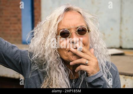 Belle femme avec de longs cheveux brillants bouclés femme tire sur une cigarette. Banque D'Images