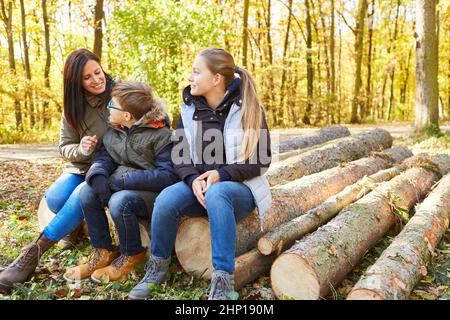 Deux enfants et une mère s'asseyent sur les troncs d'arbres lors d'une excursion dans la nature dans la forêt Banque D'Images