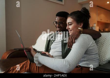 Couple biracial assis sur un canapé dactylographiant sur un ordinateur portable Banque D'Images