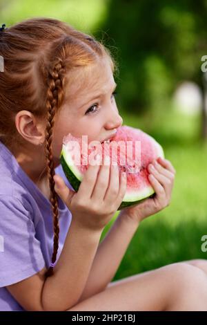 une petite fille mignonne mange une pastèque par beau temps d'été Banque D'Images