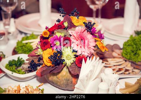 Décoration de mariage d'automne de style rustique avec fleurs et citrouilles sur les tables des invités dans le restaurant lors d'un banquet festif. Arrangeurs de fleurs de table Banque D'Images