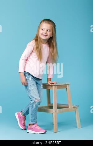 Belle petite fille en jeans et pull rose posing in studio Banque D'Images