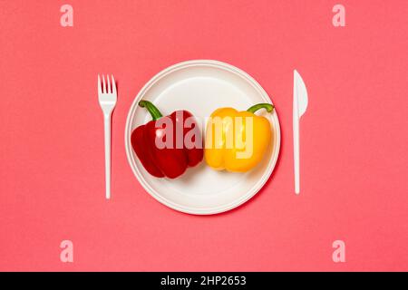 Poivron rouge et jaune sur une assiette blanche, fourchette et couteau, dieting, concept alimentaire sain.Concept créatif de la nourriture.Vue de dessus Plain d'arrière-plan rose avec Banque D'Images