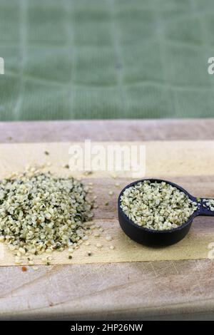 Planche à découper en bois avec des graines de chanvre décortiquées organiques également appelé coeurs de chanvre dans un tas et une cuillerée à soupe de mesure. Les graines de chanvre biologique sans coquille entendent Banque D'Images