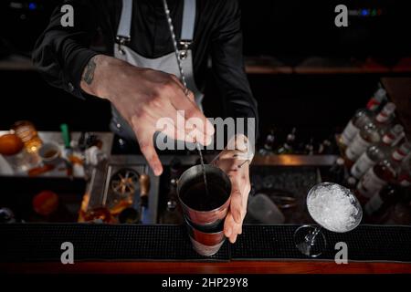 Barman en tablier, cocktail en shaker avec cuillère au bar, vue du dessus Banque D'Images