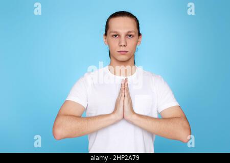 homme calme tenant les mains dans le geste de yoga, relaxant méditant, essayant de se calmer sur fond bleu Banque D'Images