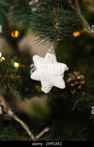 Décorations de Noël, une étoile blanche de jouet avec des sparkles est suspendue sur l'arbre, lumière chaude.Gros plan Banque D'Images