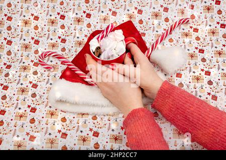 Coupe rouge avec marshmello, chapeau rouge, sucettes de Noël, bâton de cannelle et branches de sapin. Traditions de Noël Banque D'Images