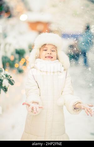 Une petite fille souriante à la foire des lumières scindonne et se réjouit. Jouer avec la neige. Banque D'Images