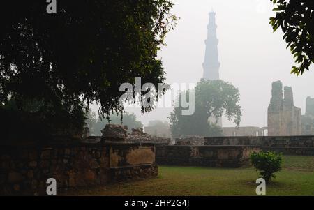 Qutb Minar le matin brumeux vu de l'intérieur des jardins historiques et des ruines flanquées d'arbres à Delhi, Inida. Banque D'Images