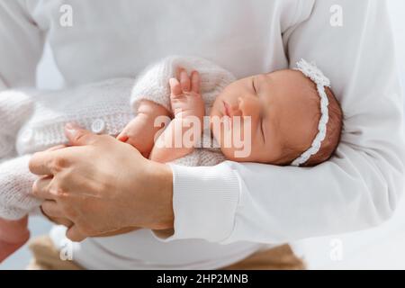 Bébé nouveau-né en costume blanc tricoté dormir sur les mains du père. Papa et fille. Petit enfant avec serre-tête tendre. Concept de Happy parenthood, lo Banque D'Images