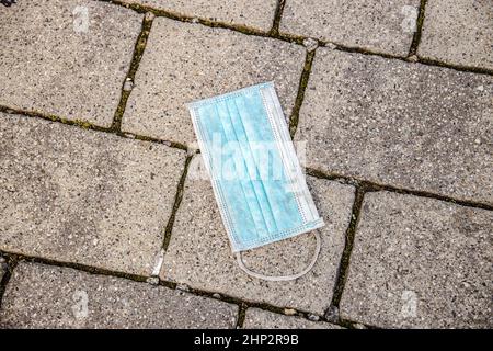 Masque médical sur le trottoir.Jeter un masque de visage usagé loin dans la rue est faux. Banque D'Images