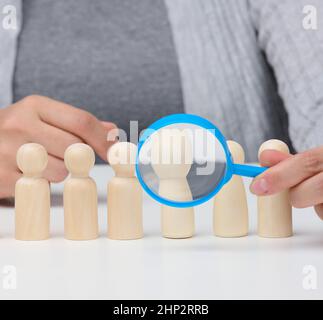 figurines d'hommes sur une table blanche, une main femelle tient une loupe sur une. concept de recherche d'employés dans l'entreprise, recrutement de pers Banque D'Images