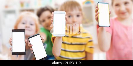 Groupe d'enfants tenant dans leurs mains smartphones avec écran maquette à l'intérieur. Concept de l'utilisation de nouvelles technologies. Banque D'Images