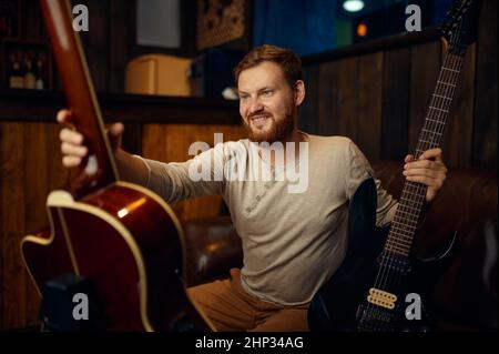 Jeune guitariste masculin qui choisit un instrument de musique entre guitare électrique ou acoustique pour jouer Banque D'Images