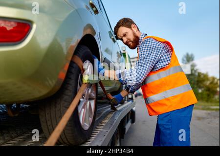 L'opérateur du chariot de remorquage fixe la voiture morte sur la plate-forme.Homme travaillant avec un véhicule en panne Banque D'Images