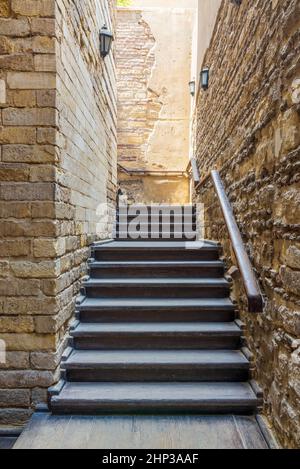 Détail architectural de l'extérieur en bois ancien abîmé escalier étroit s'accroché avec main courante en bois, entre deux murs de briques de pierre, dans le buil abandonné Banque D'Images