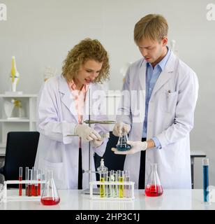 Un scientifique ukrainien ajuste soigneusement le statif et la pince pour une expérience en laboratoire.Jeune scientifique brésilien tenant Erlenmeyer flacon avec b Banque D'Images