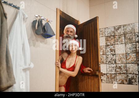 Le Père Noël et la neige en chapeau rouge donnent sur la porte du bain de vapeur. Reposez-vous dans le sauna. Vacances de Noël Banque D'Images