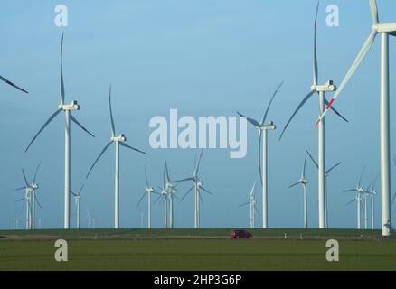 PRODUCTION - 07 février 2022, Schleswig-Holstein, Reußenköge : une voiture rouge passe devant les éoliennes. Photo: Marcus Brandt/dpa Banque D'Images