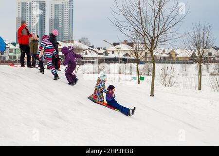 Les enfants adorables se traînaient et s'amusaient dans la neige. Un petit enfant glisse rapidement sur un traîneau. Crier avec joie. Banque D'Images