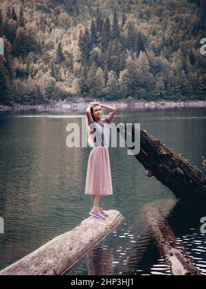 Une femme aux cheveux longs se tient sur une bûche qui se trouve dans un lac forestier près d'un grand tronc d'arbre brisé sortant de l'eau. Réserve naturelle nationale Banque D'Images