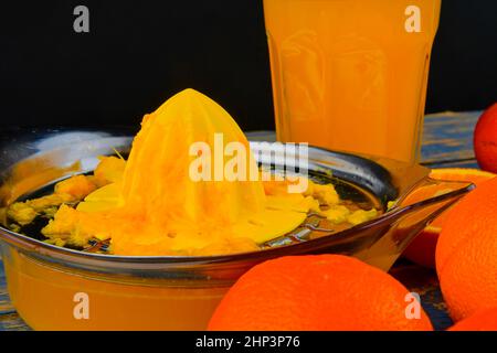 Mandarines, oranges, un verre de jus d'orange et un racloir manuel aux agrumes sur fond bleu en bois. Oranges coupées en deux. Banque D'Images