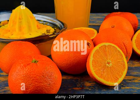 Mandarines, oranges, un verre de jus d'orange et un racloir manuel aux agrumes sur fond bleu en bois. Oranges coupées en deux. Banque D'Images