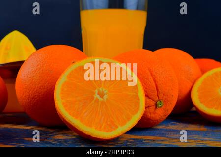 Mandarines, oranges, un verre de jus d'orange et un racloir manuel aux agrumes sur fond bleu en bois. Oranges coupées en deux. Banque D'Images