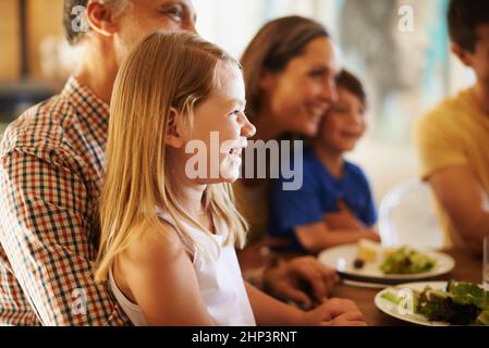 Le circuit des grands-pads est la position principale. Photo d'une petite fille assise sur les genoux de ses grands-pères au dîner avec sa famille en arrière-plan. Banque D'Images